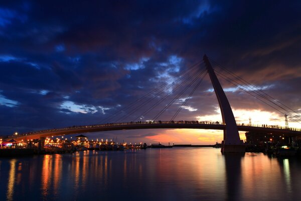 A huge bridge with people standing on it, a river and ships below