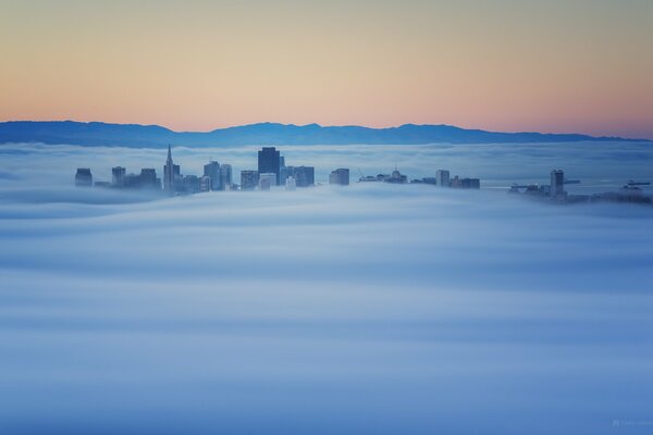 Le cime degli edifici sbirciano dalla nebbia