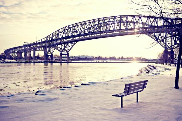 View of the bridge, river and bench in the snow