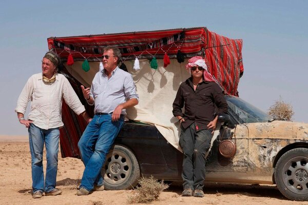 Three guys are standing near a car in the desert