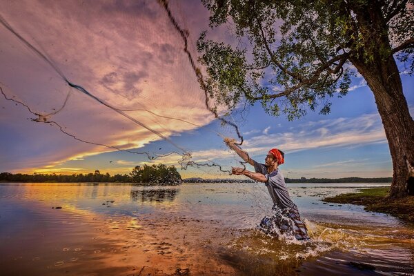 A fisherman catches fish with a net at sunset