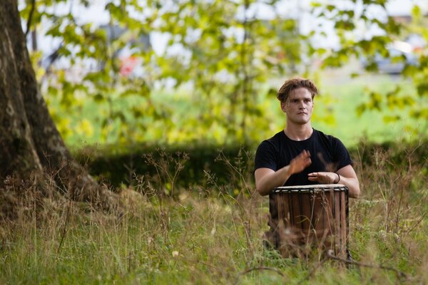 A man on the lawn beats a drum