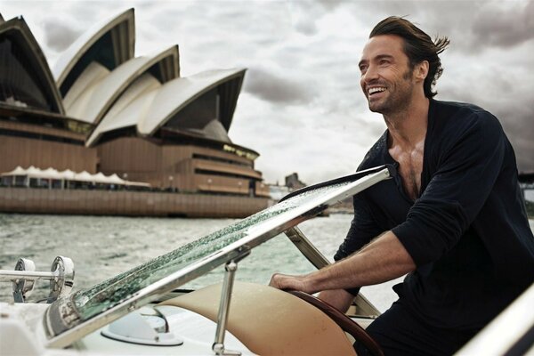 El actor Hugh Jackman en una bata sonríe desde un barco