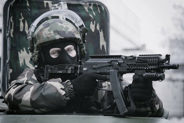 A masked special forces soldier shoots from a machine gun