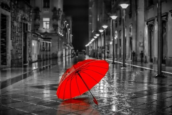 Un parapluie rouge vif se trouve sur l asphalte mouillé par la pluie au milieu de l allée grise de la ville de nuit