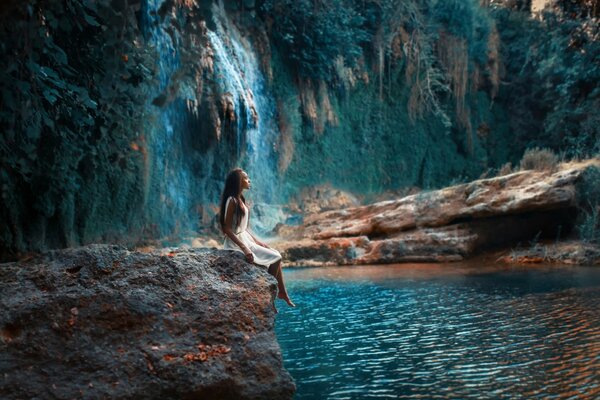 Bella ragazza sulla pietra alla cascata