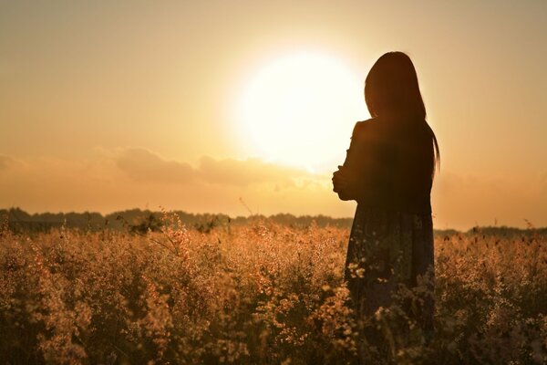 Einsames Mädchen vor dem Hintergrund des Sonnenuntergangs und der Blumen