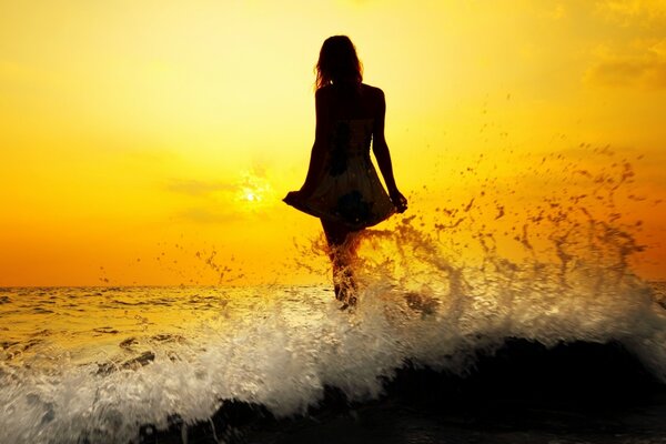 A girl stands in the water and looks at the sunset