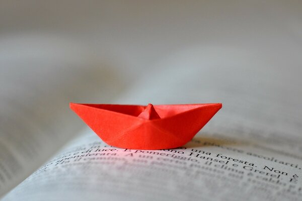 A red paper boat lies on the leaves of an open book