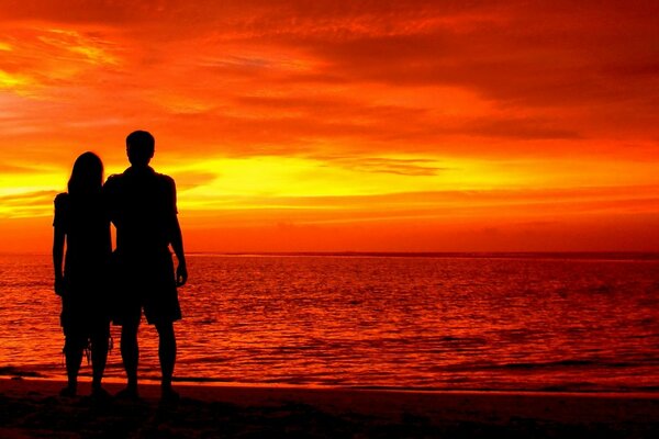 A man and a woman standing on the shore at sunset