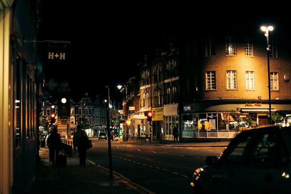 Menschen, die auf dem Bürgersteig laufen und Autos neben der Straße in London bei Abendlicht vorbeifahren