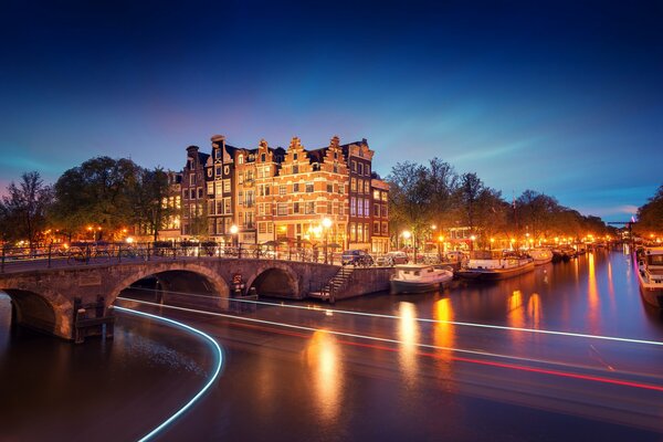 Houses and boats on the canals of Amsterdam with lights on the water against the background of the evening transparent sky