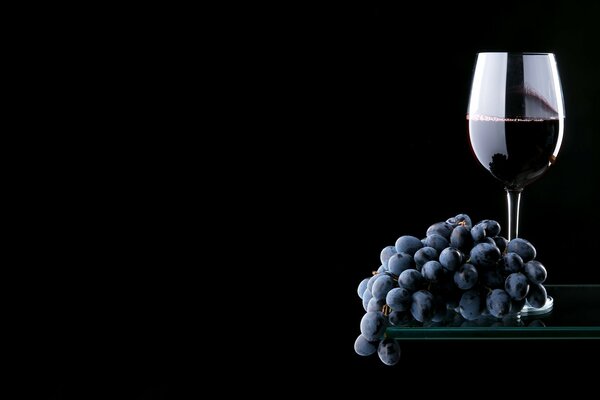 Vino tinto con un racimo de uvas sobre un fondo negro