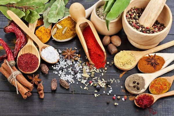 Spices in wooden bowls and spoons on a dark countertop