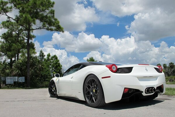 Śnieżnobiałe Ferrari na tle błękitnego nieba i tych samych śnieżnobiałych chmur