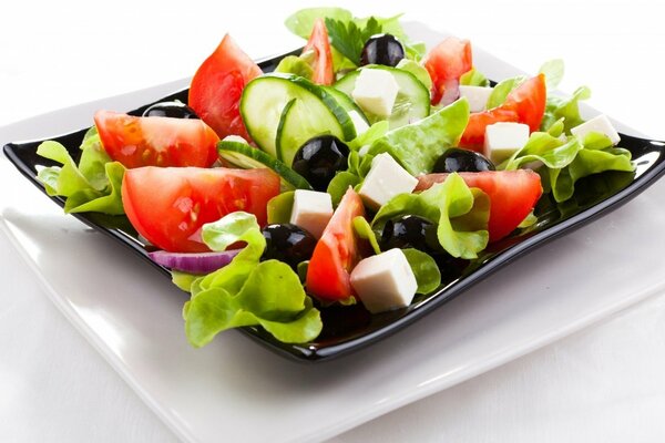 Greek salad in a black plate on a white plate