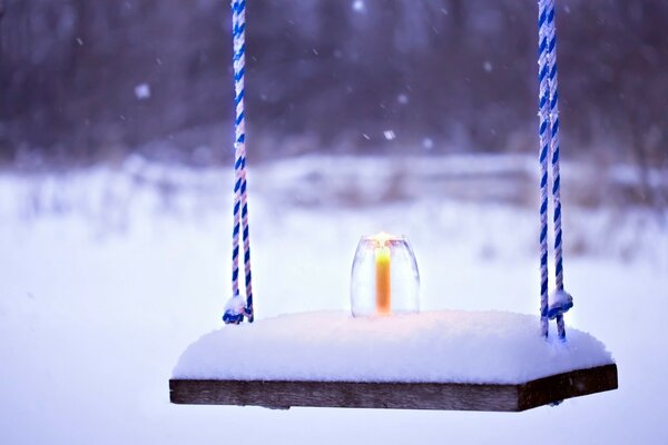 Paesaggio innevato, altalena nella neve, candela accesa nella neve