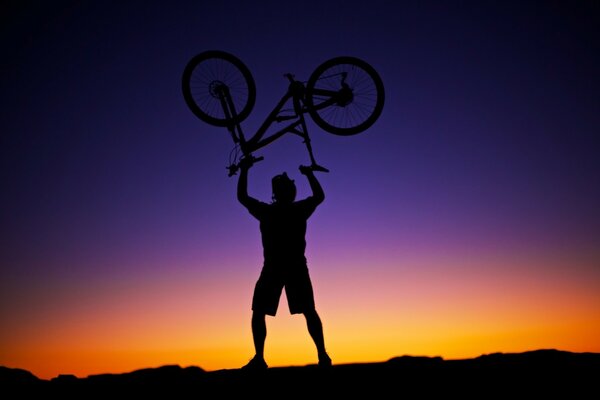 Homme levé vélo sur fond de coucher de soleil, beau ciel