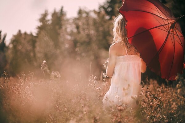 Fille en robe blanche et avec un parapluie rouge parmi les fleurs