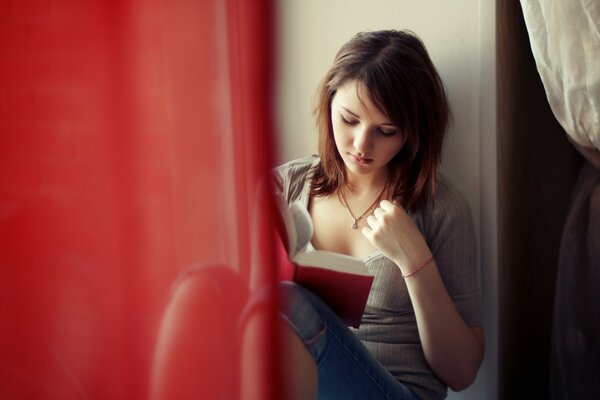 La jeune fille assise près de la fenêtre lit un livre