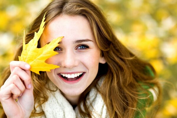 A positive girl covers her face with an autumn leaf