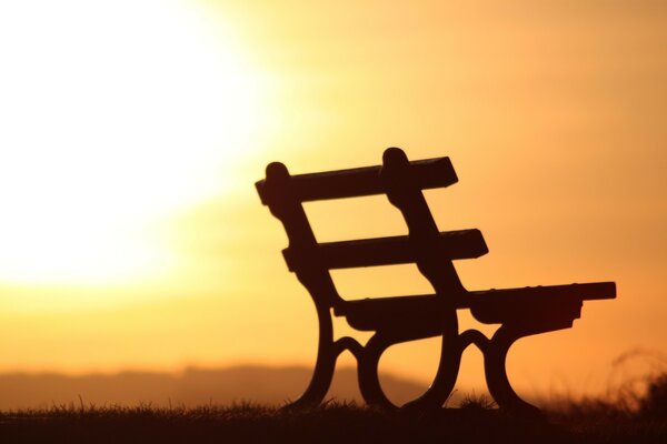 The silhouette of a bench against the background of an orange sunset