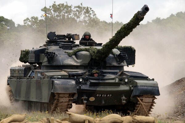 A tank with a gun raised high rides over rough terrain