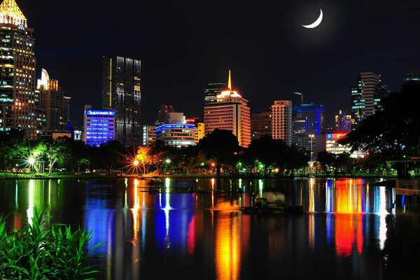 Las luces nocturnas de la ciudad se reflejan en el agua y un mes cuelga en el cielo