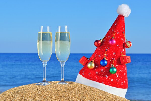 Christmas hat with champagne glasses on the sand