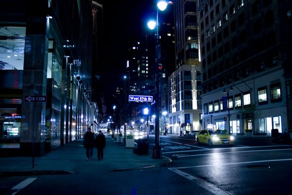 People are walking, a taxi is driving along a quiet night street