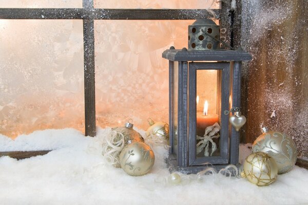 Linterna con velas en la ventana cubierta de nieve