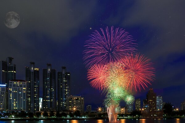 Colored fireworks on the background of the moonlit sky and the city