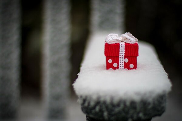 Un pequeño regalo lindo en una tienda cubierta de nieve en el parque. Caja de regalo roja