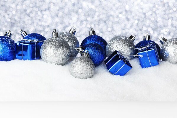 Silver-blue Christmas tree toys lie on the snow on a silver sparkling background