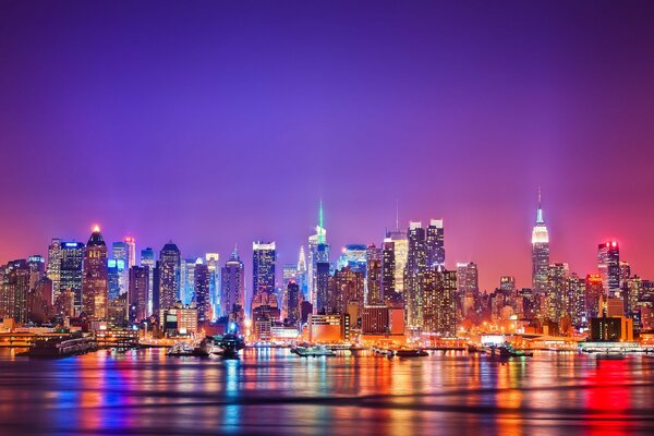 The lights of Manhattan at night are reflected in the Hudson River