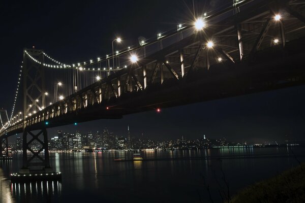 The bright night lights on the bridge are reflected in the river