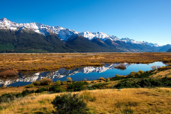 A steppe lake and snow-capped mountains are mirrored in it