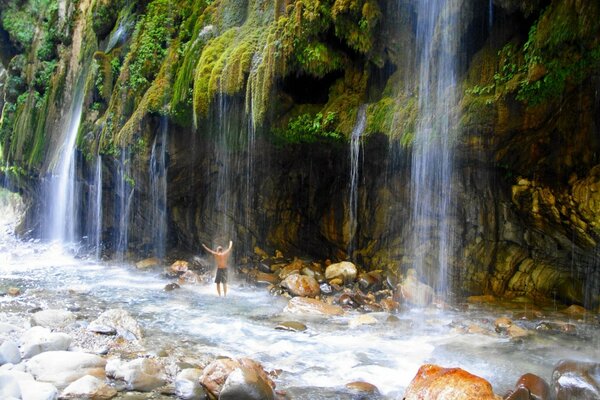 A man stands under a waterfall in Greece