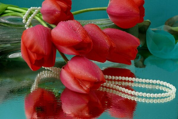 Red tulips wrapped in a pearl necklace lie on a glossy table