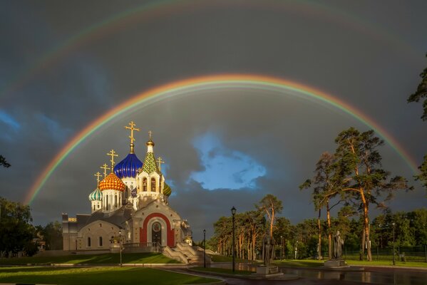 Двойная радуга на церковью среди деревьев