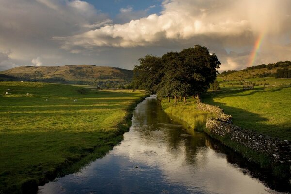 Nature rainbow in the river against the background of mountains and fields