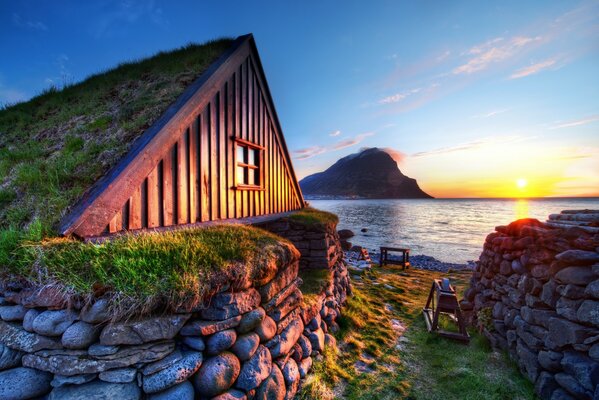 Pequeña casa de madera en la orilla del río iluminada por la puesta de sol