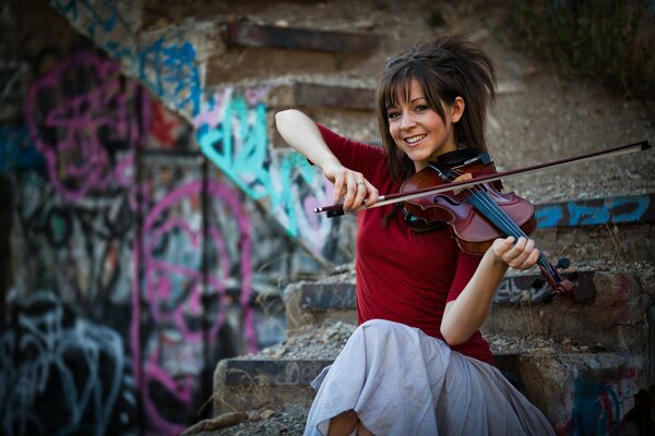 Lindsay Stirling tocando el violín en el fondo de una escalera pintada de graffiti