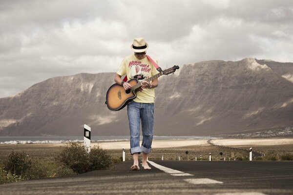 Chico guitarrista caminando por la carretera en medio de las montañas