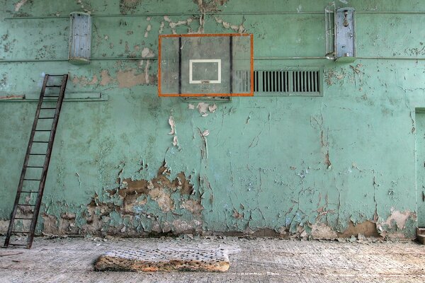 Eine verlassene Turnhalle, eine Wand in abgestorbener Farbe, eine verfallene Matte auf dem Boden