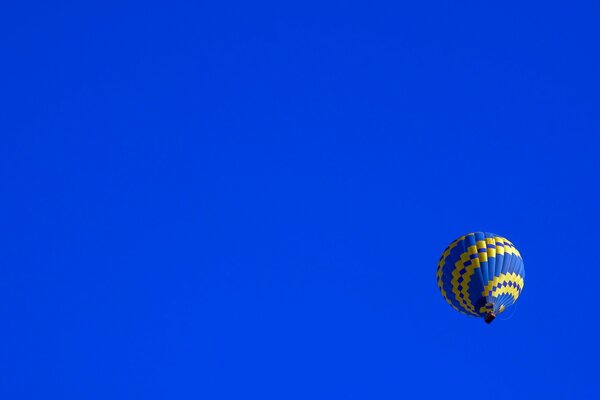 A blue-yellow balloon slowly flies across the sky