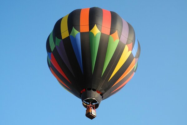 A multicolored balloon is flying against a blue sky background