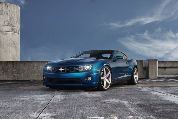 Una chevrolet Camaro blu si trova in un parcheggio contro uno splendido cielo