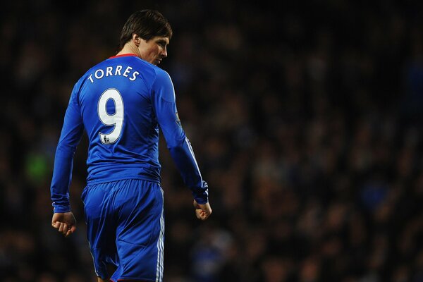 A football player in a blue uniform walks thoughtfully in front of the stands with the audience