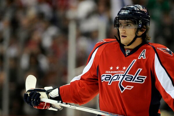 Un joueur de hockey en uniforme rouge tient un bâton blanc dans ses mains